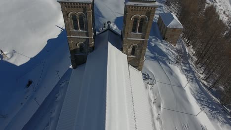 Nahaufnahme-Eines-Fluges-über-Eine-Verschneite-Kirche-Und-Ein-Heiligtum.-Drohnenschuss-Aus-Frankreich